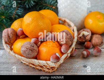 Les tangerines et les noix dans un panier en osier sur l'arrière-plan de branches de sapin. Noël. Nouvelle année. Selective focus Banque D'Images