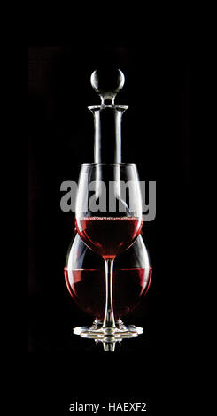 Dans un verre de vin rouge se trouve en face d'une carafe de vin rouge. Le verre noir. Isolé sur le noir. Banque D'Images