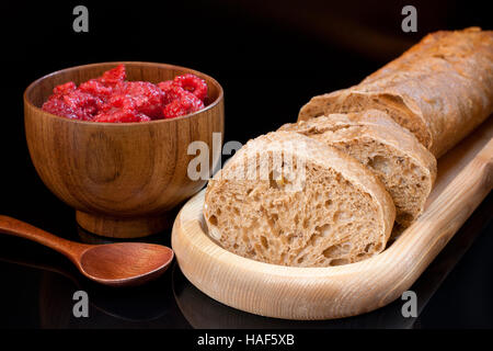 Plaque en bois avec des tranches de pain et une tasse de framboises et cuillère couché sur le tableau sur fond noir. Banque D'Images