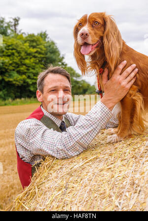 Un homme avec un cocker assis sur le ballot de paille sur un jour d'été Banque D'Images