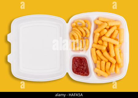 Vue de dessus de la malbouffe ingrédients et un plongeon de ketchup dans une boîte d'emballage à emporter blanc sur fond jaune, les calories concept Banque D'Images