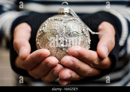 Closeup of a young man wearing mittens tenant une boule de noël ornée confortable Banque D'Images