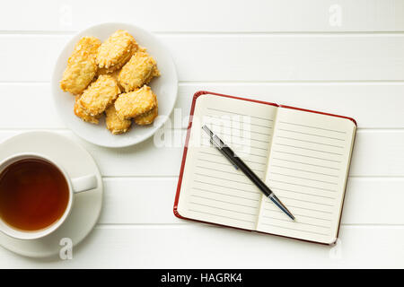 Le bloc-notes avec stylo blanc et des biscuits avec du thé. Vue d'en haut. Banque D'Images