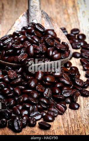 Grains de café dans une cuillère de bois sur fond de bois. Banque D'Images