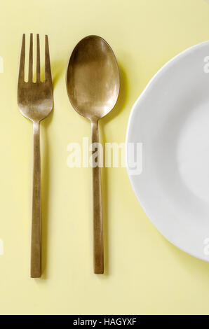 Fourchette et cuillère en laiton , plat blanc sur fond jaune Banque D'Images