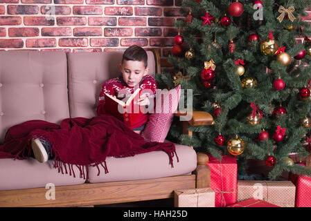 Le garçon est assis sur une chaise et la lecture d'un livre Banque D'Images