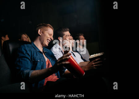 Jeune homme avec des amis en salle de cinéma à regarder film et rire. Groupe de personnes regarder la vidéo dans le théâtre. Banque D'Images