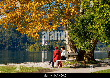 Deux amis sur un banc de parc avec l'église Sainte-Marie de l'Assomption, au-delà de la Haute-Carniole, Bled, Slovénie Banque D'Images