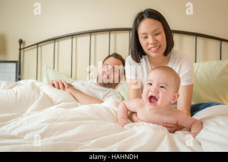 Young mixed race caucasienne et Chinois Baby Boy Laying In Bed avec son père et sa mère. Banque D'Images