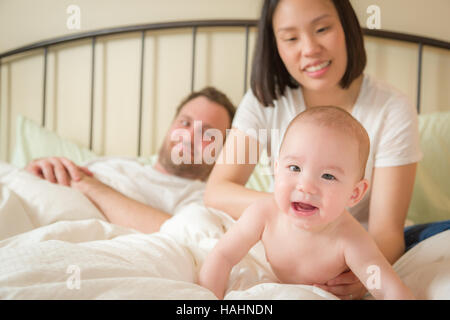 Young mixed race caucasienne et Chinois Baby Boy Laying In Bed avec son père et sa mère. Banque D'Images