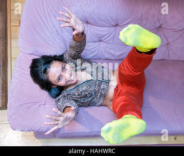 Cheerful girl enjoué sur le canapé, vue du dessus. La femme s'étend ses mains et jambes. Asian woman lying on bed with jambes et mains, regardez ci-dessus. Banque D'Images