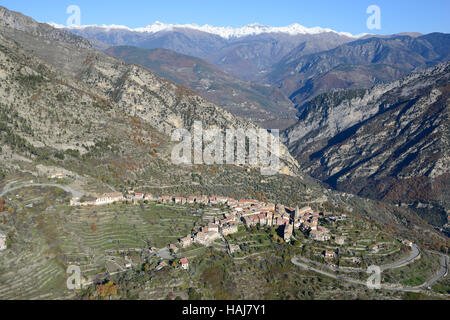 VUE AÉRIENNE. Village perché surplombant la vallée de la Vésubie avec les Alpes enneigées du Mercantour au loin. Utelle, Alpes-Maritimes, France. Banque D'Images