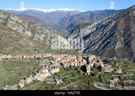 VUE AÉRIENNE. Village perché surplombant la vallée de la Vésubie avec les Alpes enneigées du Mercantour au loin. Utelle, Alpes-Maritimes, France. Banque D'Images