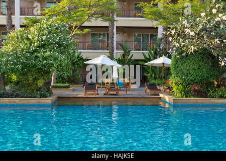 Chaises longues au bord de la piscine dans la verdure tropicale. Banque D'Images