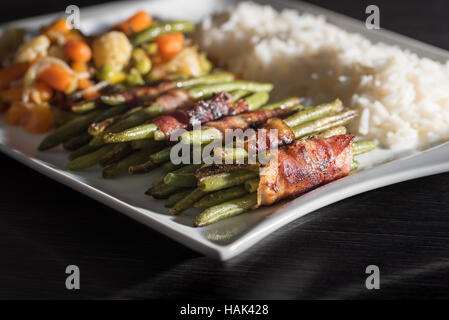 Bas Carb - Haricots verts enrobé de bacon avec un mélange de légumes et de riz blanc sur plaque. Banque D'Images