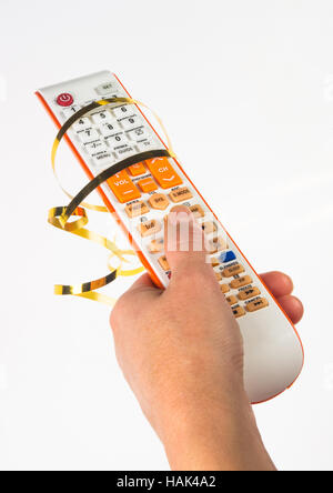 Main tenant une télécommande dans un ruban d'or de fête sur fond blanc Banque D'Images