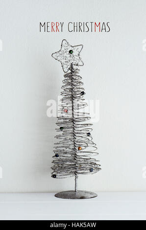 La simplification de l'arbre de Noël en fil métallique placé sur une surface blanche, contre un mur blanc et le texte joyeux noël Banque D'Images