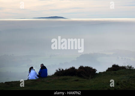 Couple assis au sommet de la colline Wrekin dans Shropshire avec la gorge Severn enveloppé dans le brouillard d'automne ci-dessous et les Brown Clee hill peeping tu Banque D'Images