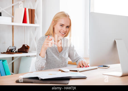 Portrait of a young smiling business woman travail avec ordinateur et montre de l'index at camera Banque D'Images