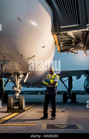 Travailleur de l'équipe au sol de l'aéroport avec presse-papiers en vertu de l'avion sur le tarmac Banque D'Images