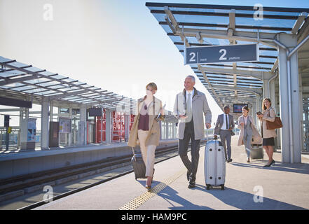 Business people walking tirant valises sur la plate-forme de la gare ensoleillée Banque D'Images