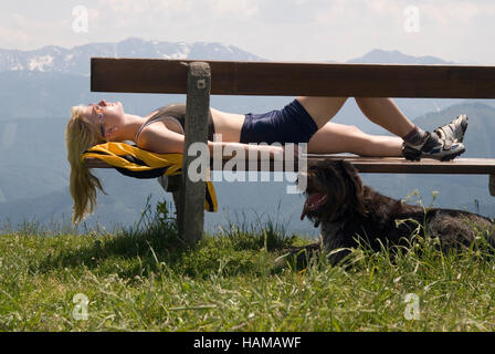 Jeune femme allongée sur un banc à côté de son chien, en prenant une pause de sa randonnée pédestre Banque D'Images