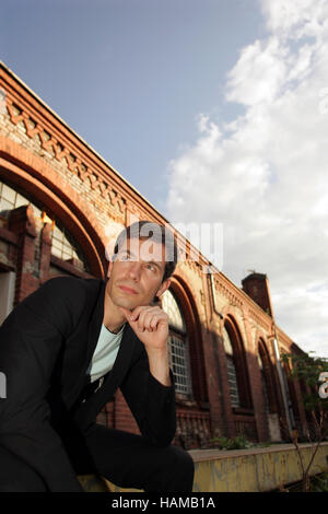 Portrait d'un jeune homme portant un costume, assis en face d'un bâtiment industriel en briques rouges à la recherche dans la distance Banque D'Images