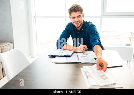 Photo de jeune homme soie joyeuse de l'analyse de la situation financière et la tenue de journal à la main. Banque D'Images