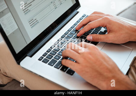 Portrait of a young man's hands typing sur son ordinateur portable tandis que l'homme assis sur un canapé. Banque D'Images