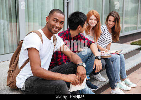Happy african american étudiant jeune homme assis avec ses frieds outdoors Banque D'Images