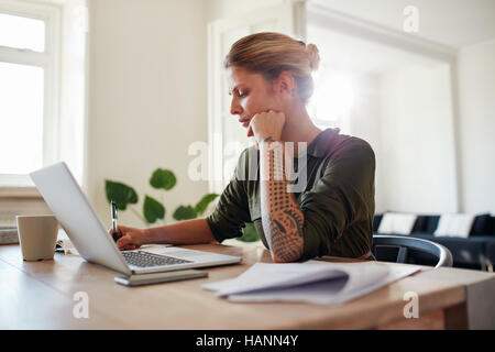 Coup de jeune femme travaillant au bureau à domicile. Belle femme assise à table avec ordinateur portable et documents. Banque D'Images