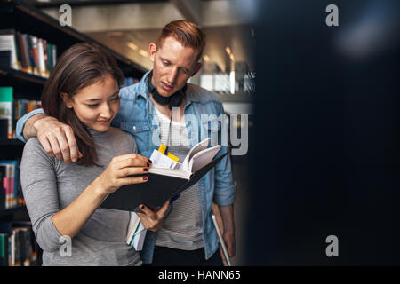 Les jeunes étudiants à trouver des ouvrages de référence en bibliothèque universitaire. L'homme et la femme university students standing par bibliothèque en bibliothèque et lire un livre. Banque D'Images