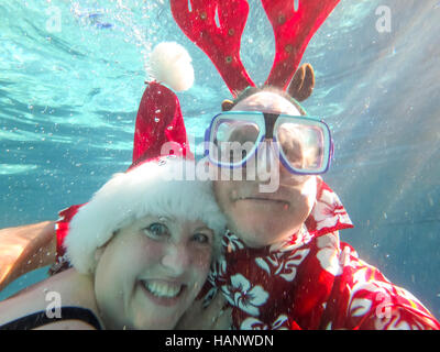 Couple in Santa hat et oreilles de rennes sous l'eau. Banque D'Images