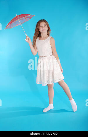 Cheerful young girl en robe blanche avec un parapluie debout contre le fond bleu Banque D'Images