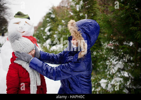 La femme avec la petite fille sur la marche en hiver 24. Froid. Pour la mère corrige soigneusement tricotés fille un PAC. Bonhomme de neige dans un chapeau et un foulard Banque D'Images