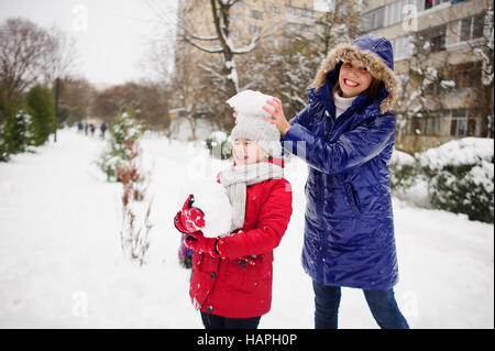 Jeune femme et sa fille nom de passer du temps sur la rue en journée d'hiver. Ils sont vêtus de manteaux chauds. Terre est couverte de neige. Maman met sur Banque D'Images