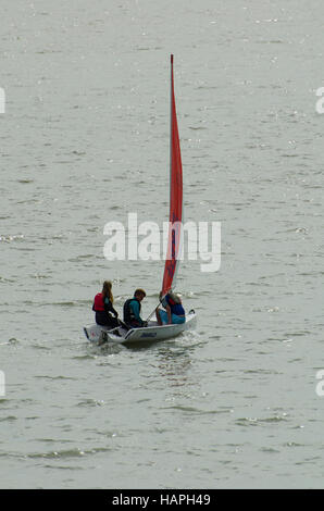 Un petit canot voile contenant trois jeunes sur la mer. Banque D'Images