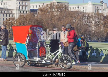 Londres, Westminster Bridge un cycle tuk-tuk avec son red-clad 'Driver' et les badauds Banque D'Images