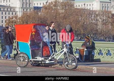 Londres, Westminster Bridge un cycle tuk-tuk 'Driver' assister à ses 'TAXI' Banque D'Images