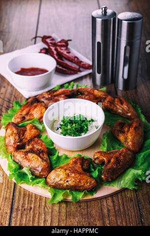 Ailes de poulet délicieux grillés à l'ail et de la sauce tomate avec de la laitue sur une carte ronde sur fond rustique en bois Banque D'Images