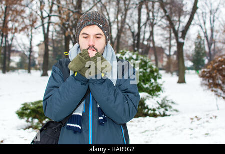 Jeune homme se réchauffer les mains dans le parc couvert de neige Banque D'Images