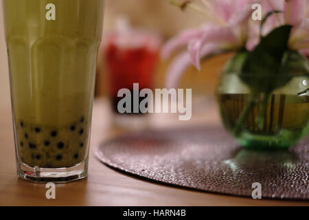 Deux grands verres de bubble tea, un vert avec une paille, en premier plan, un rouge, dans l'arrière-plan sur une table. Banque D'Images