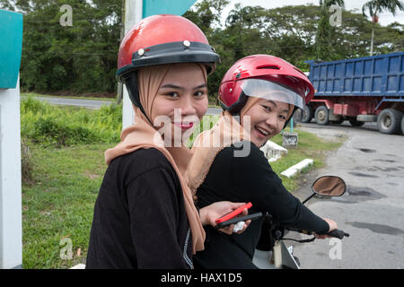 Deux filles musulmanes vêtus, assis sur un scooter à Mukah, Division de Mukah, Sarawak, Malaisie Banque D'Images