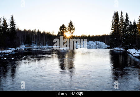 Petite rivière avec la forêt des deux côtés et le soleil de l'hiver dans l'horizon,photo du nord de la Suède. Banque D'Images