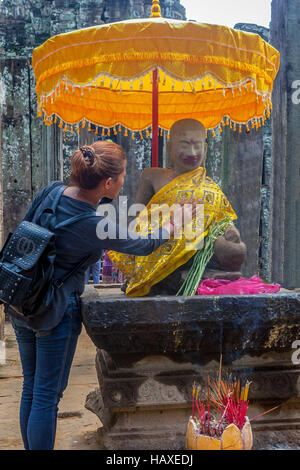 Une jeune femme met sa main sur le coeur de Bouddha à un culte dans l'ancien temple du complexe d'Angkor Thom. Banque D'Images