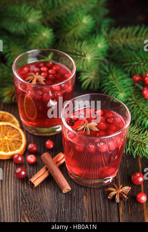 Deux verres de boissons à base de canneberge, canneberge, bâtons de cannelle, d'anis étoile et tranches d'orange séchée sur un fond de bois. Banque D'Images