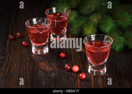 Trois verres de boissons rafraîchissantes aux fruits rouges cocktail de canneberges les canneberges et les branches de l'épinette dans l'arrière-plan sur un fond de bois. Banque D'Images
