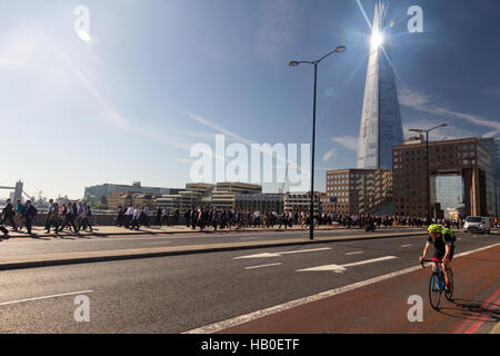 À vélo au travail à travers le pont de Londres au cours de la matinée, le trafic avec la lumière du soleil brillant sur le Shard building en arrière-plan. Banque D'Images