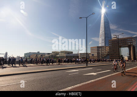 À vélo au travail à travers le pont de Londres au cours de la matinée, le trafic avec la lumière du soleil brillant sur le Shard building en arrière-plan. Banque D'Images