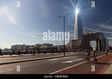 À vélo au travail à travers le pont de Londres au cours de la matinée, le trafic avec la lumière du soleil brillant sur le Shard building en arrière-plan. Banque D'Images